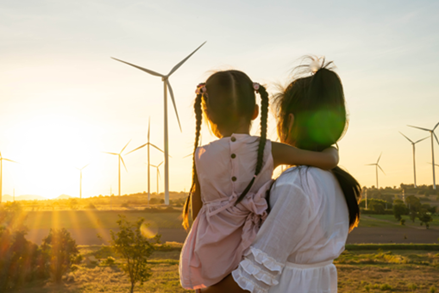 A mother and daughter look at wind turbines during sunset