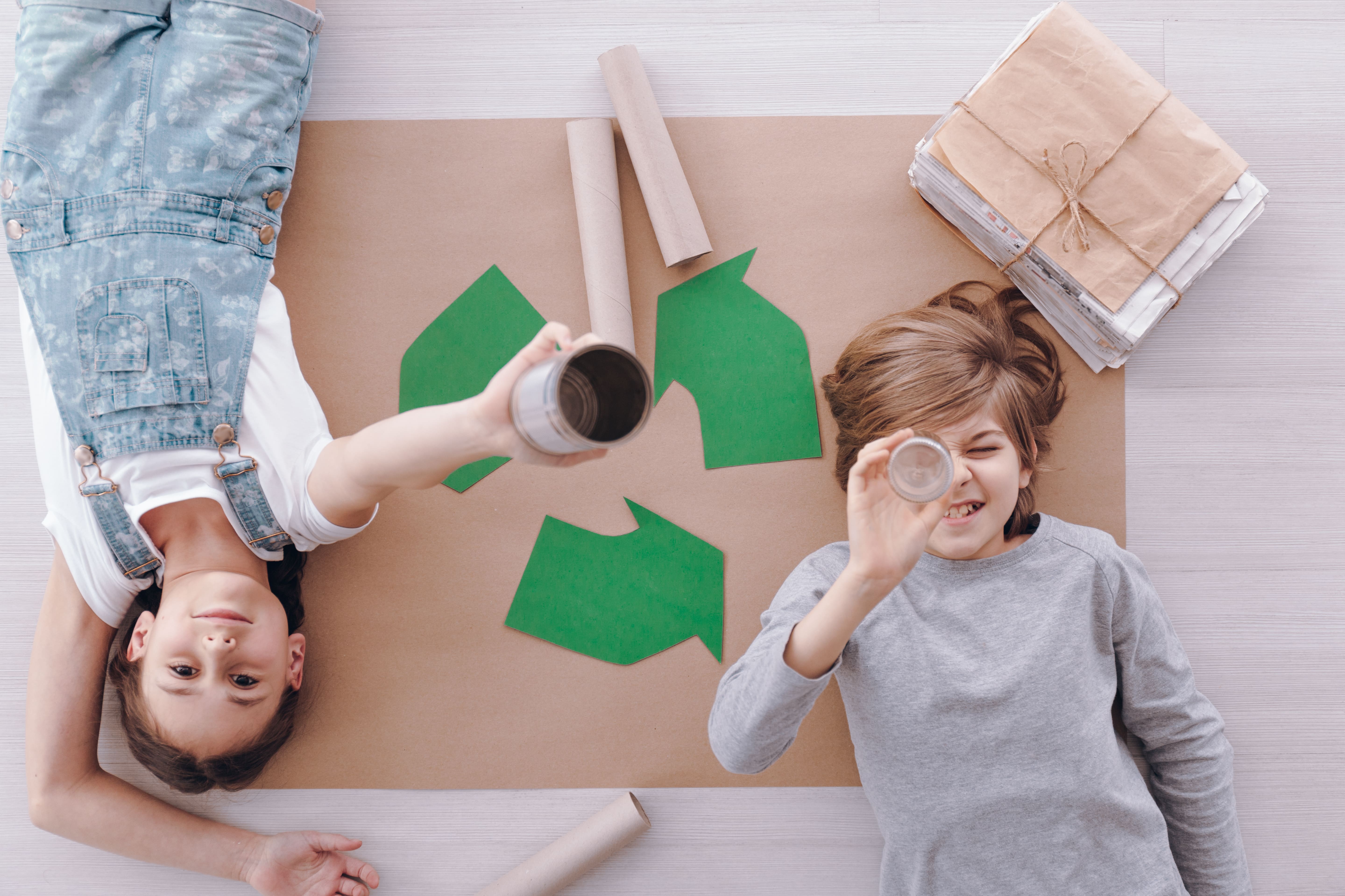 Children lying next to a recycling symbol with paper and cardboard